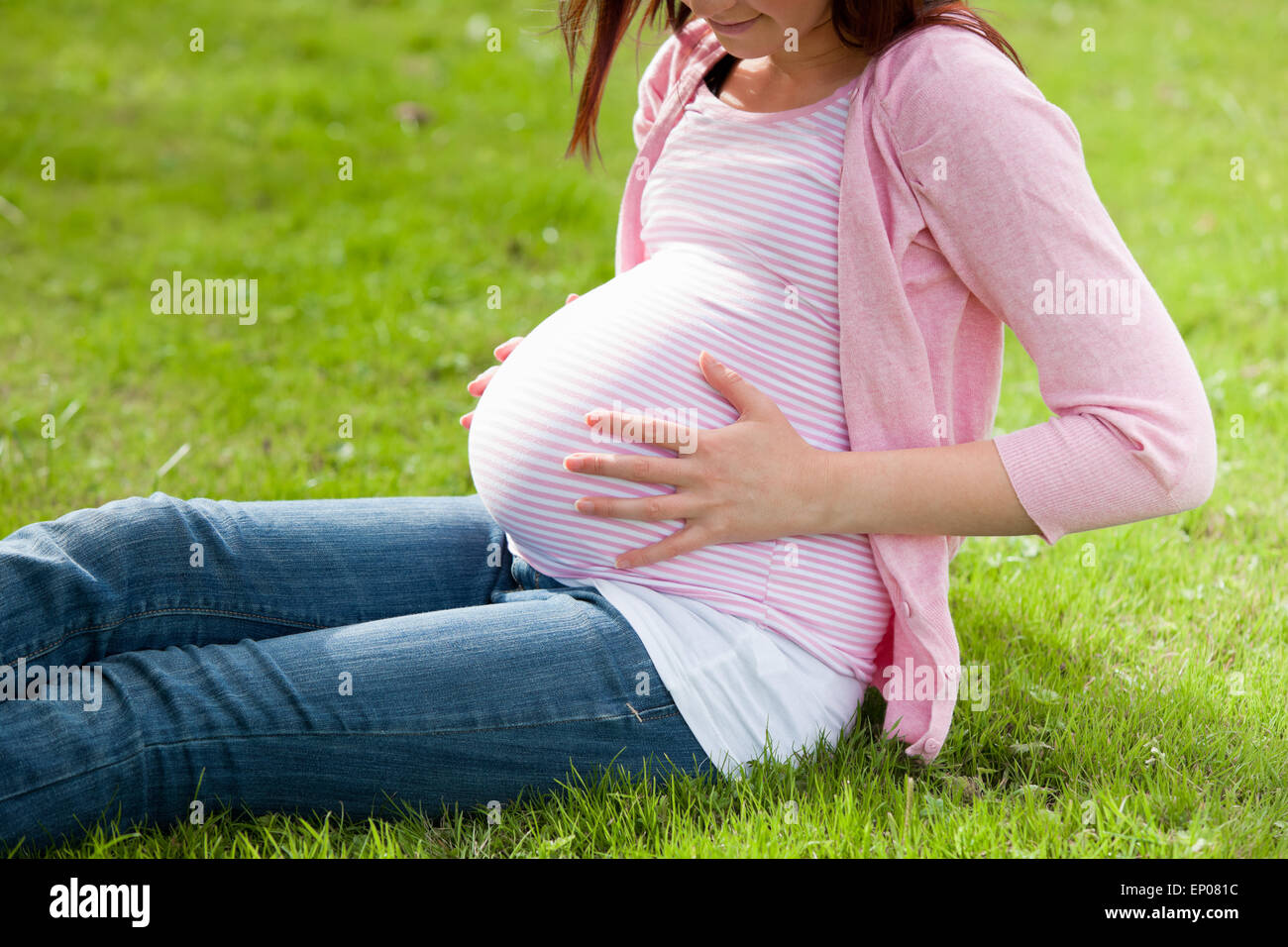 Pregnant woman holding her stomach sitting on the grass Stock Photo - Alamy