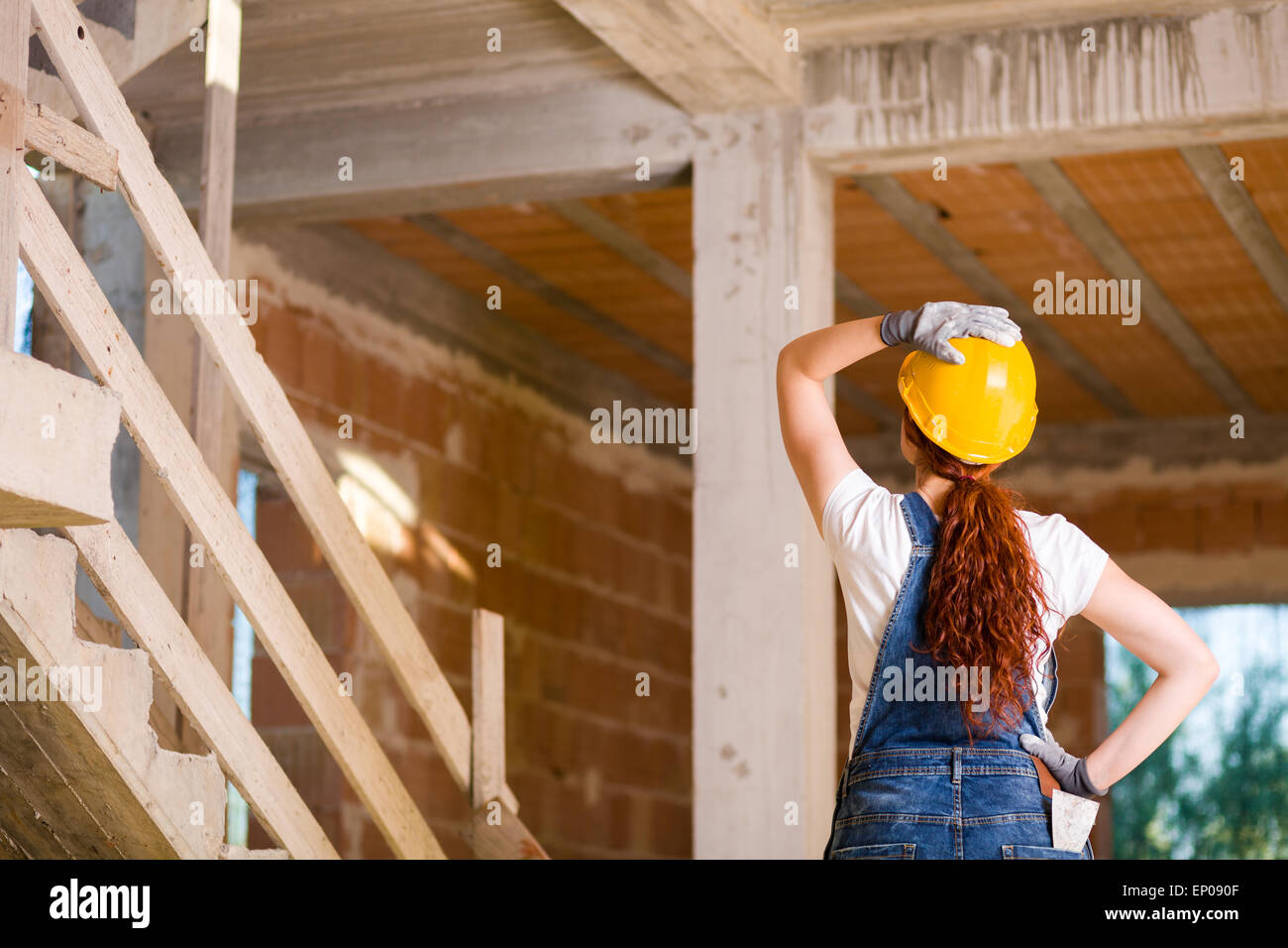 Woman Bricklayer with Overalls and Helmet Watching Upstairs Stock Photo