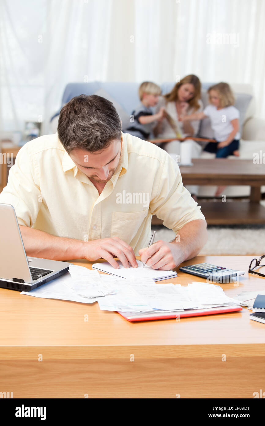 Man calculating his bills while his family are on the sofa Stock Photo