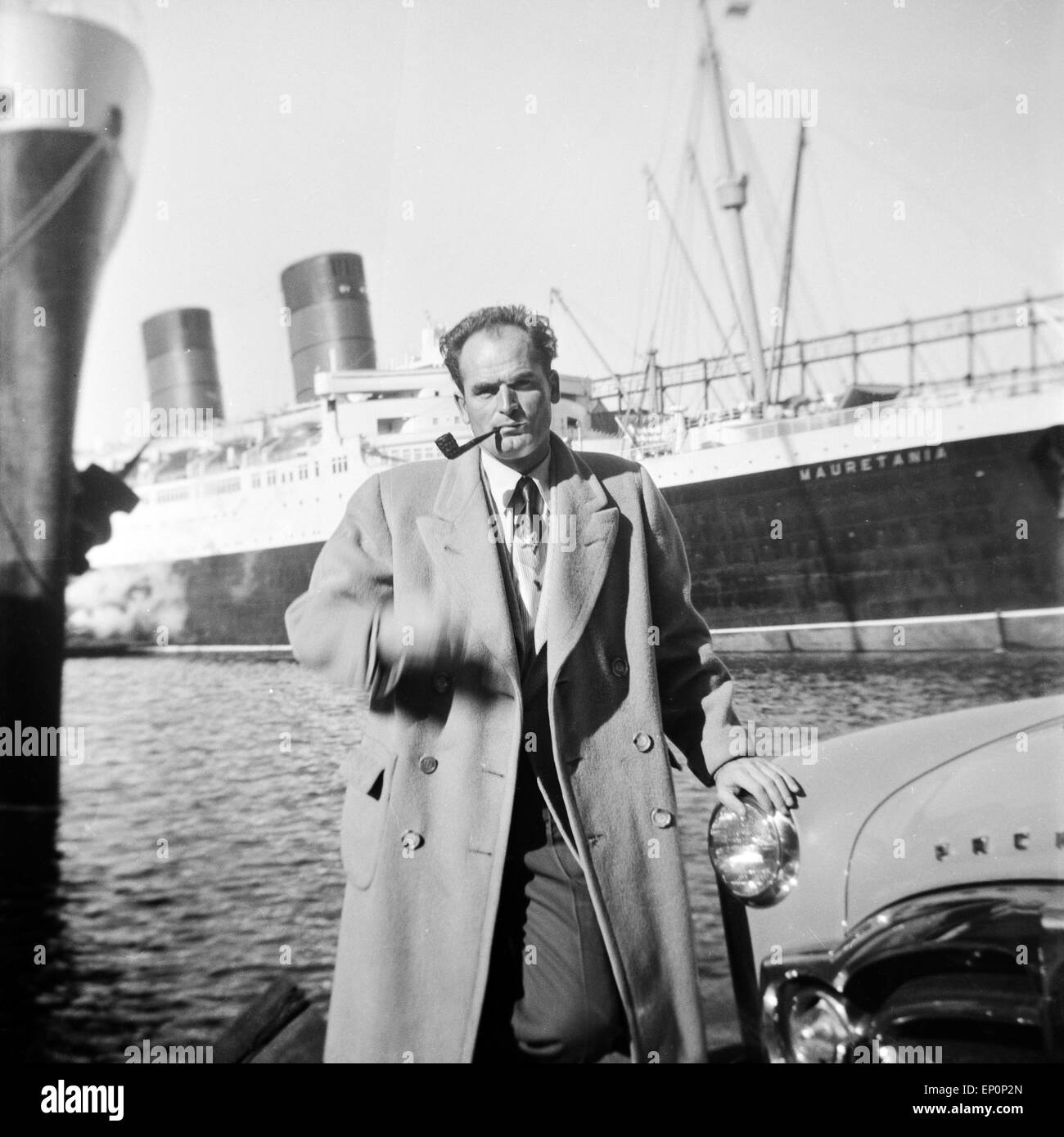 Ein Mann steht an seinem Auto der Marke Studebaker Packard im Hafen von Hamburg und raucht seine Pfeife, 1954. A man standing by Stock Photo
