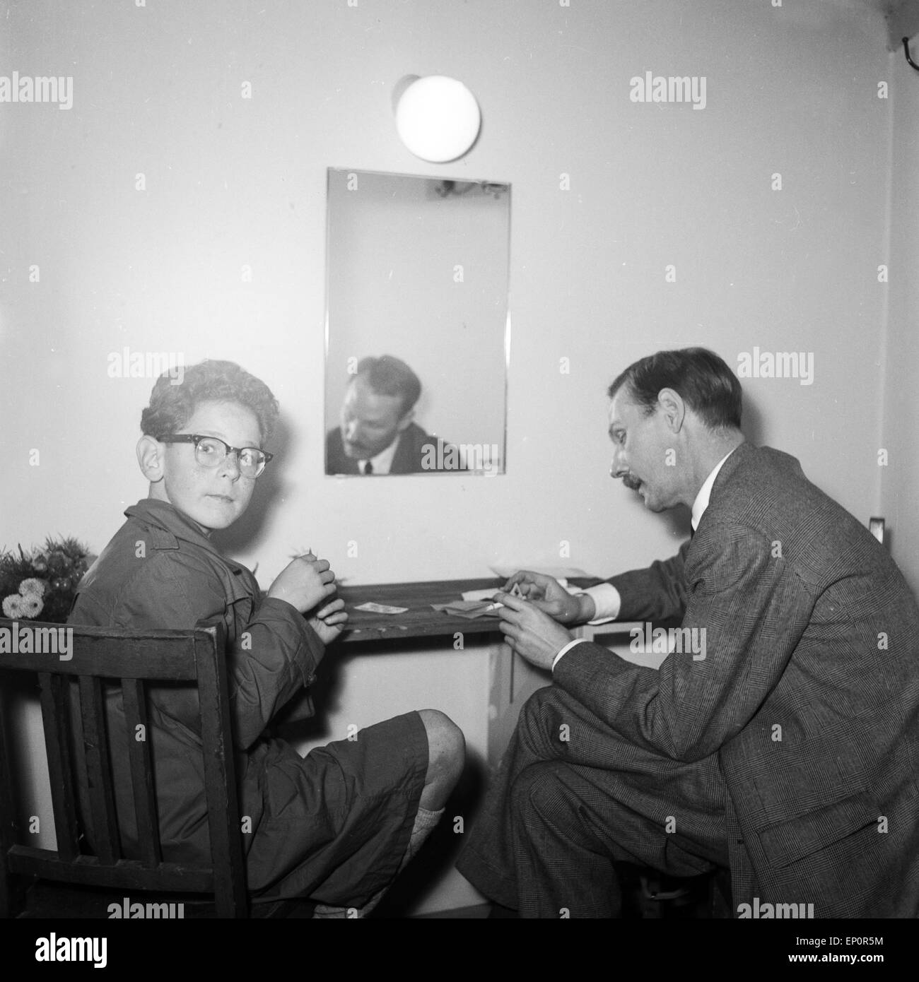 Ein Mann und ein kleiner Junge mit Brille sitzen an einem Tisch und spielen Karten, Kiel 1954. A little boy with glasses and a m Stock Photo