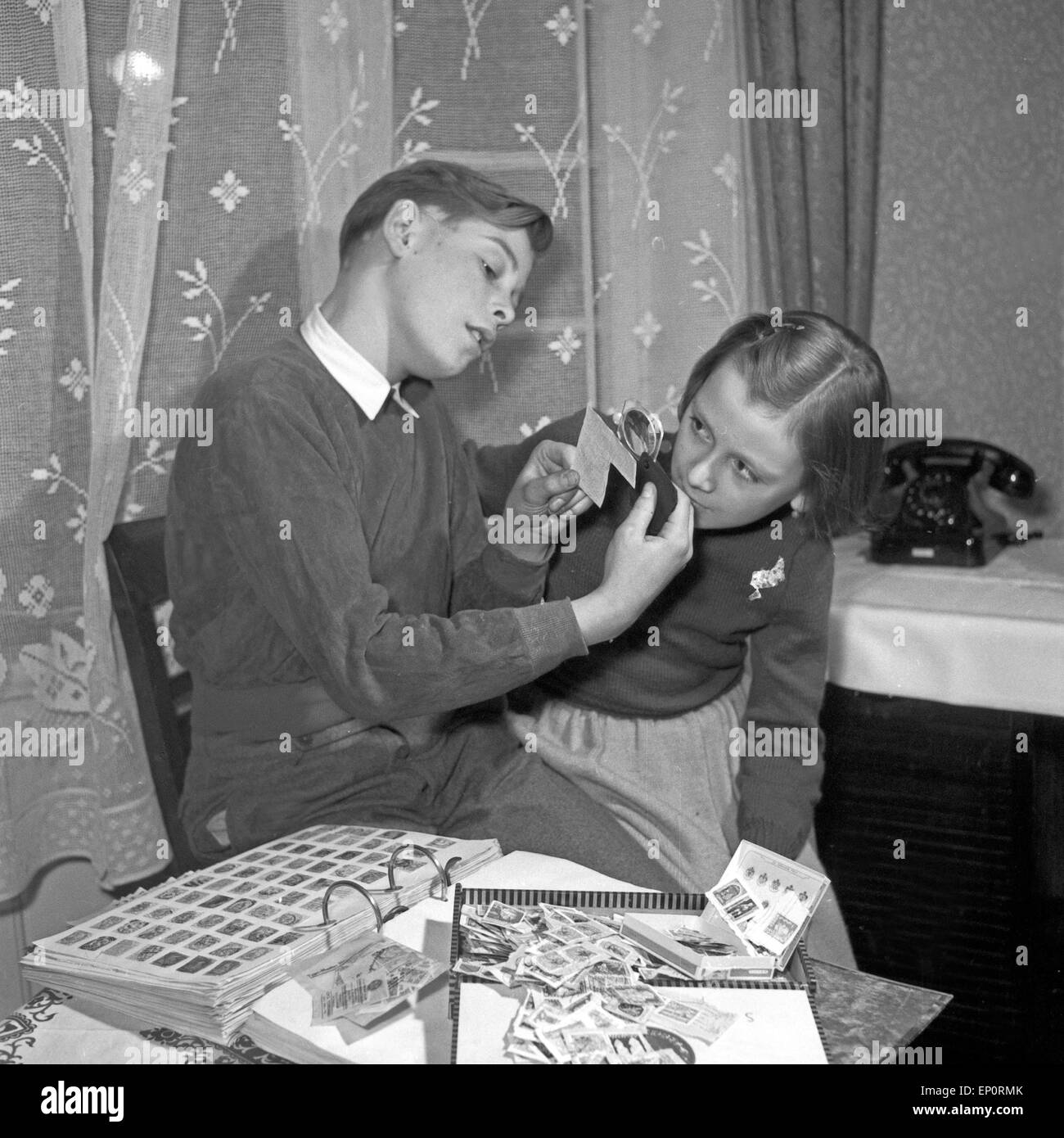 Ein Junge zeigt einem Mädchen seine Briefmarkensammlung, Deutschland 1950er Jahre. A boy showing a little girl his hobby: his st Stock Photo