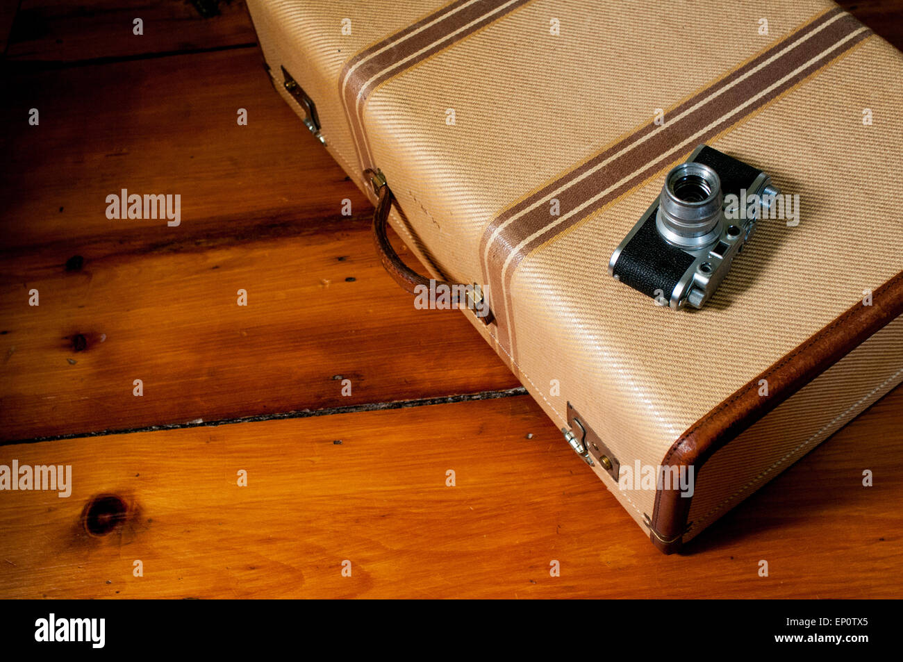 A vintage suitcase and camera sit on a wood floor. Stock Photo
