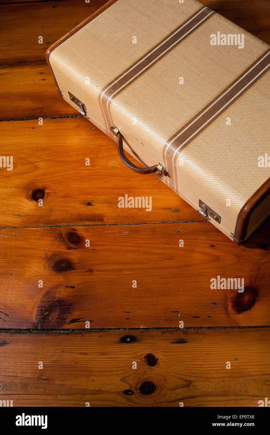 A vintage suitcase sits on a wood floor. Stock Photo
