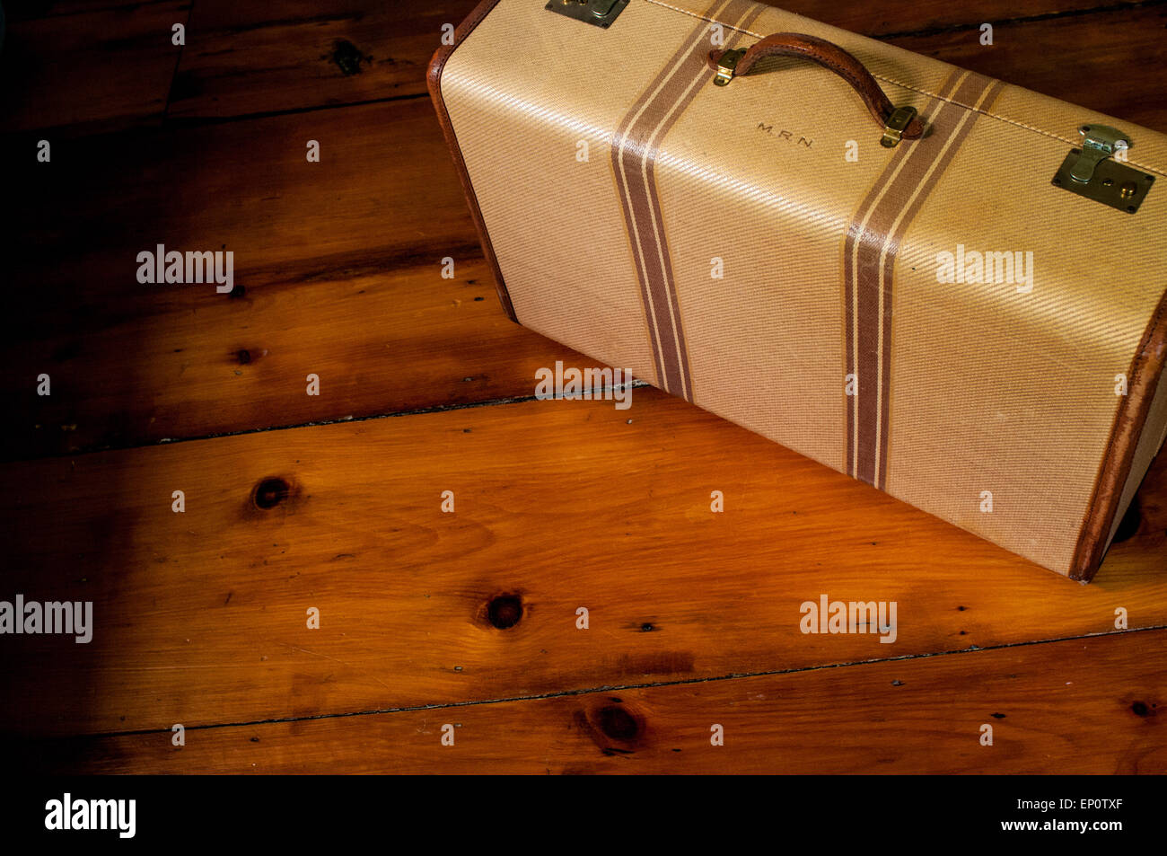 A monogrammed vintage suitcase sits on an old wood floor. Stock Photo