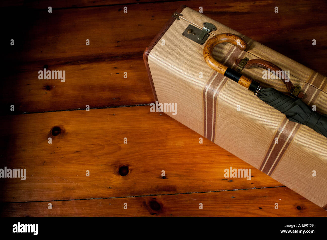 A vintage suitcase and umbrella sit on a wood floor. Stock Photo