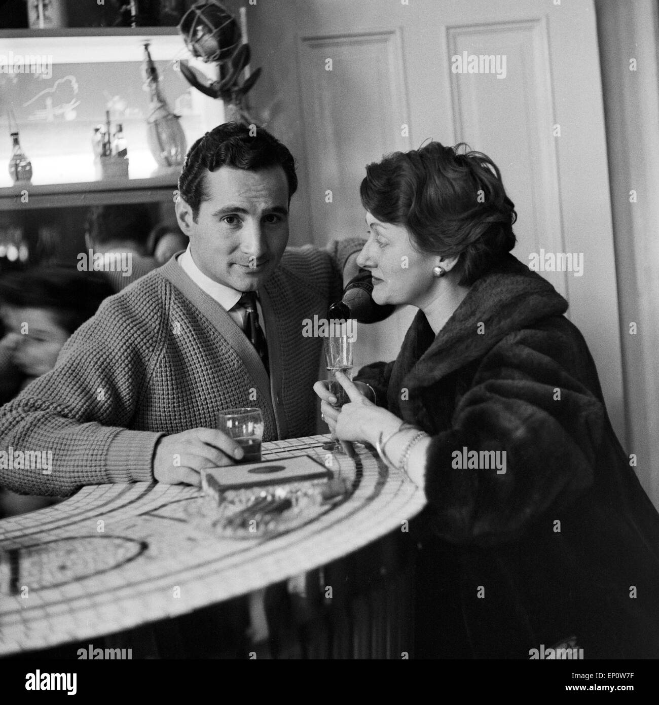 Deutscher Sänger Freddy Quinn schenkt einer Frau im Mantel ein Glas Sekt ein, ca. 1957. German singer Freddy Quinn offering a Stock Photo