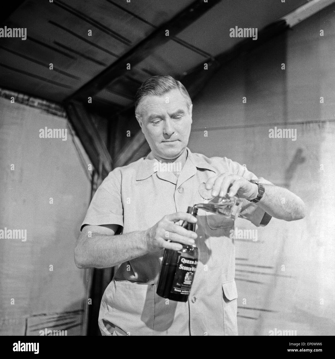 Deutscher Schauspieler Heinz Klingenberg füllt einen Whisky vom Glas zurück in die Flasche, Deutschland 1950er Jahre. Stock Photo