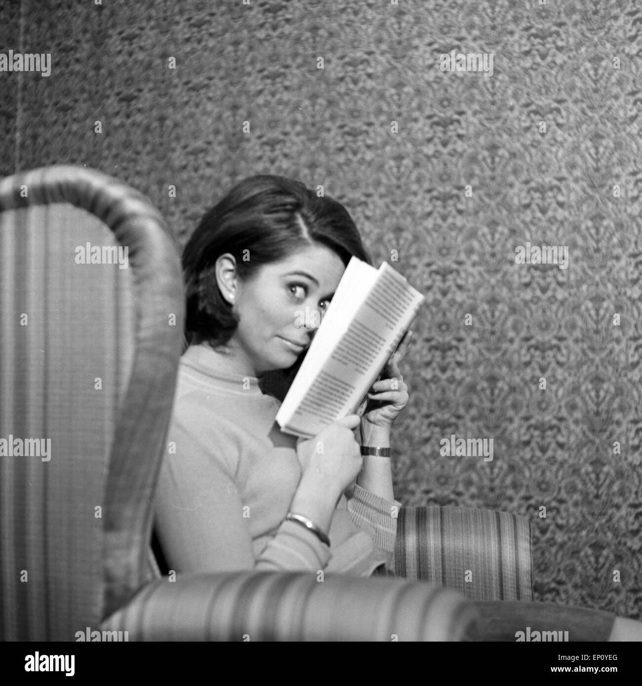 Norwegische Schlagersängerin Wencke Myhre versteckt sich im Wohnzimmersessel hinter einem Buch, 1960er Jahre. Norwegian schl Stock Photo