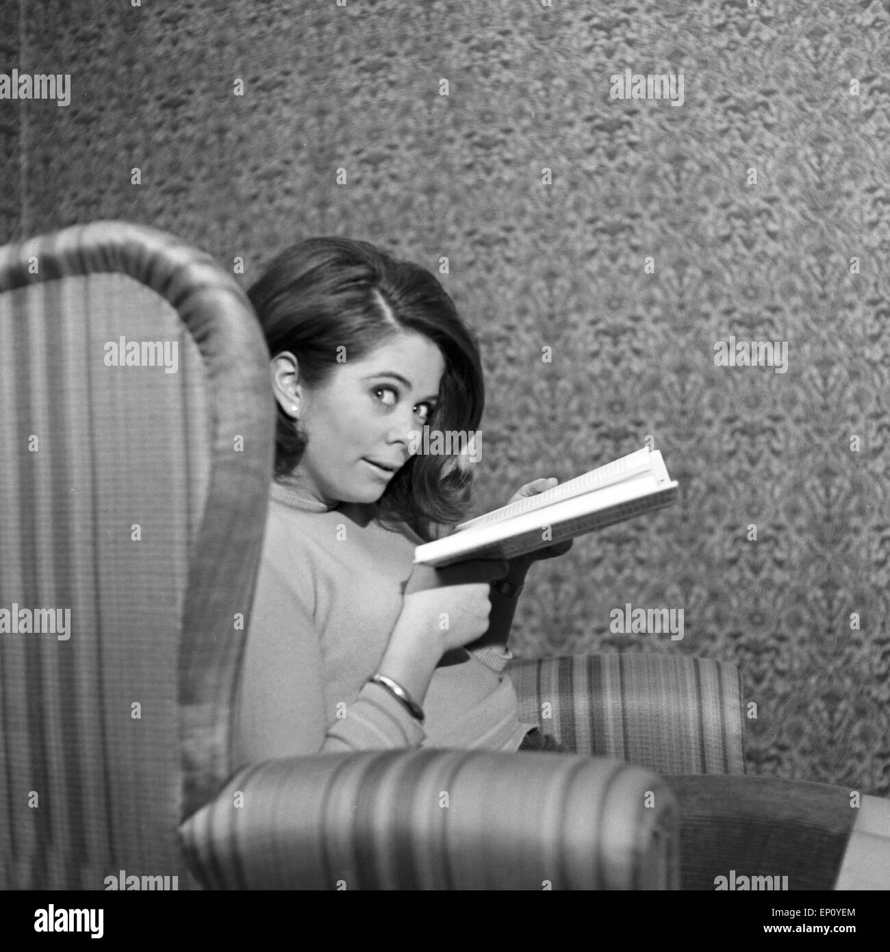 Norwegische Schlagersängerin Wencke Myhre versteckt sich im Wohnzimmersessel hinter einem Buch, 1960er Jahre. Norwegian schl Stock Photo