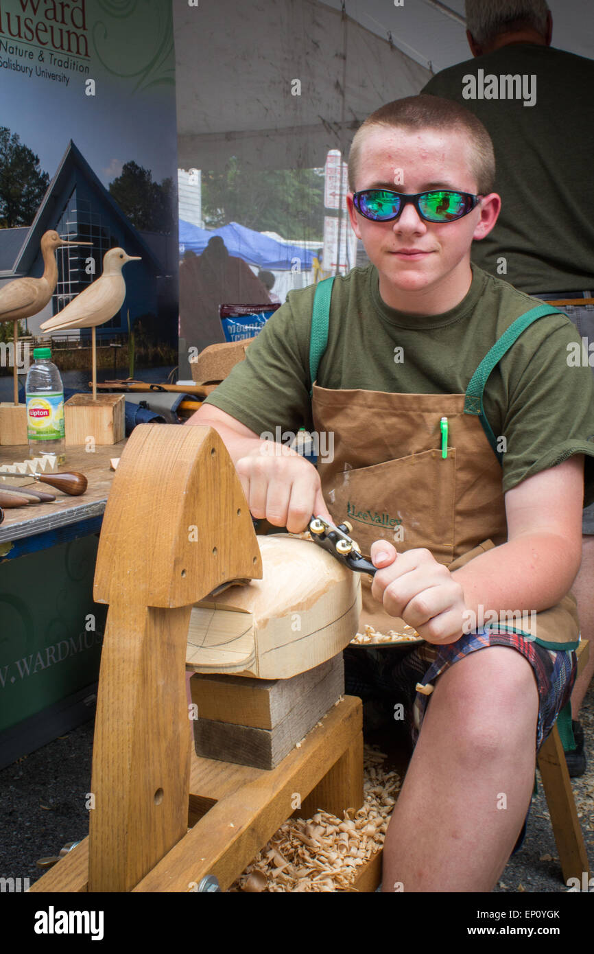 Boy wearing sunglasses carving wood, using a shaving horse in Baltimore, Maryland, USA Stock Photo