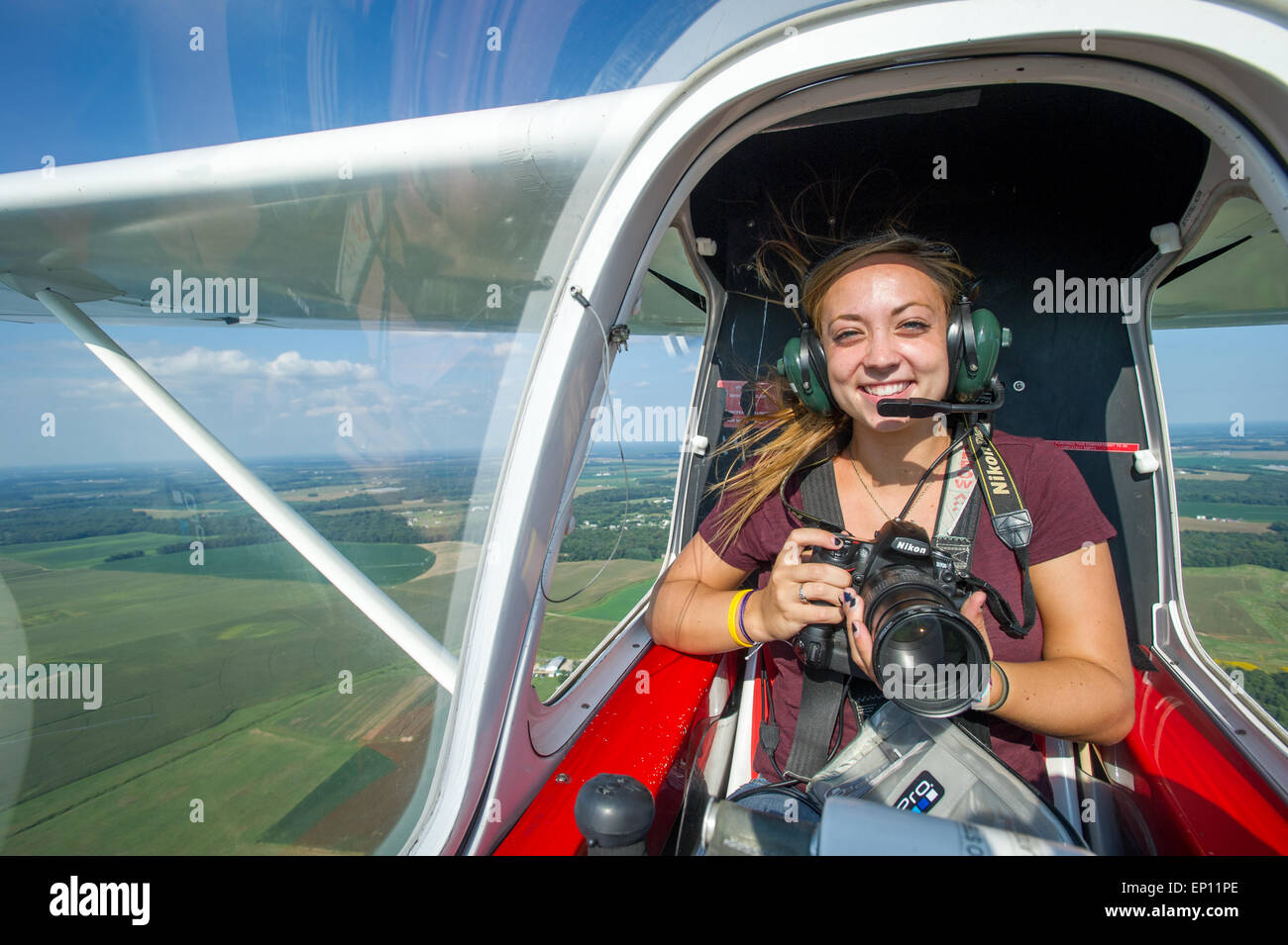 Smiling female photographer holding camera in small airplane while airborne, in Ridgley, Maryland, USA Stock Photo