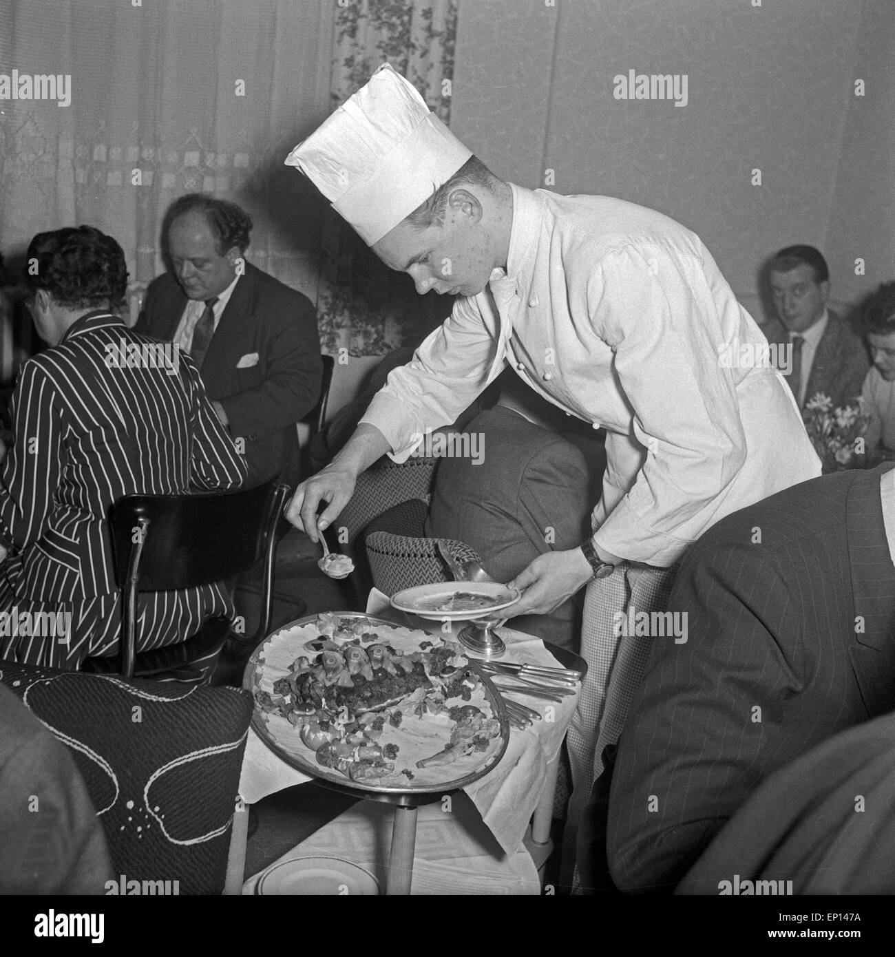Ein Koch serviert fachmännisch von einer Felischplatte, Deutschland 1950er Jahre. A chef serving from a grill dsih, Germany 1950 Stock Photo