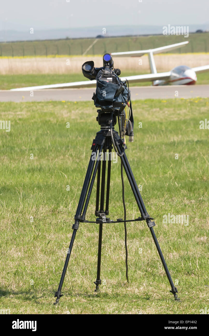 Tripod mounted video camera oriented towards a stationary glider on an airfield Stock Photo