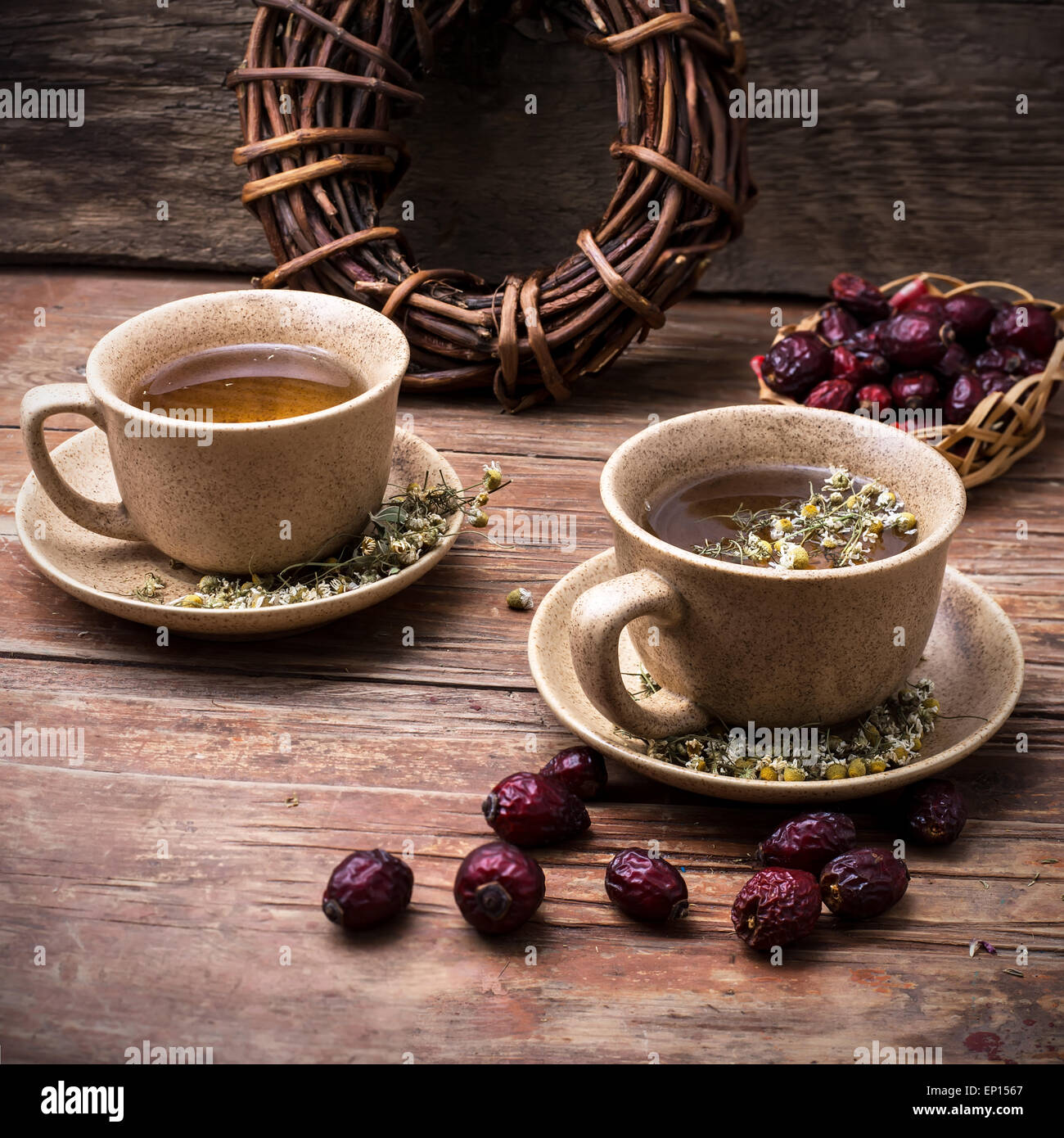 Two ceramic cups brewed tea with rosehip and chamomile amid bundles of