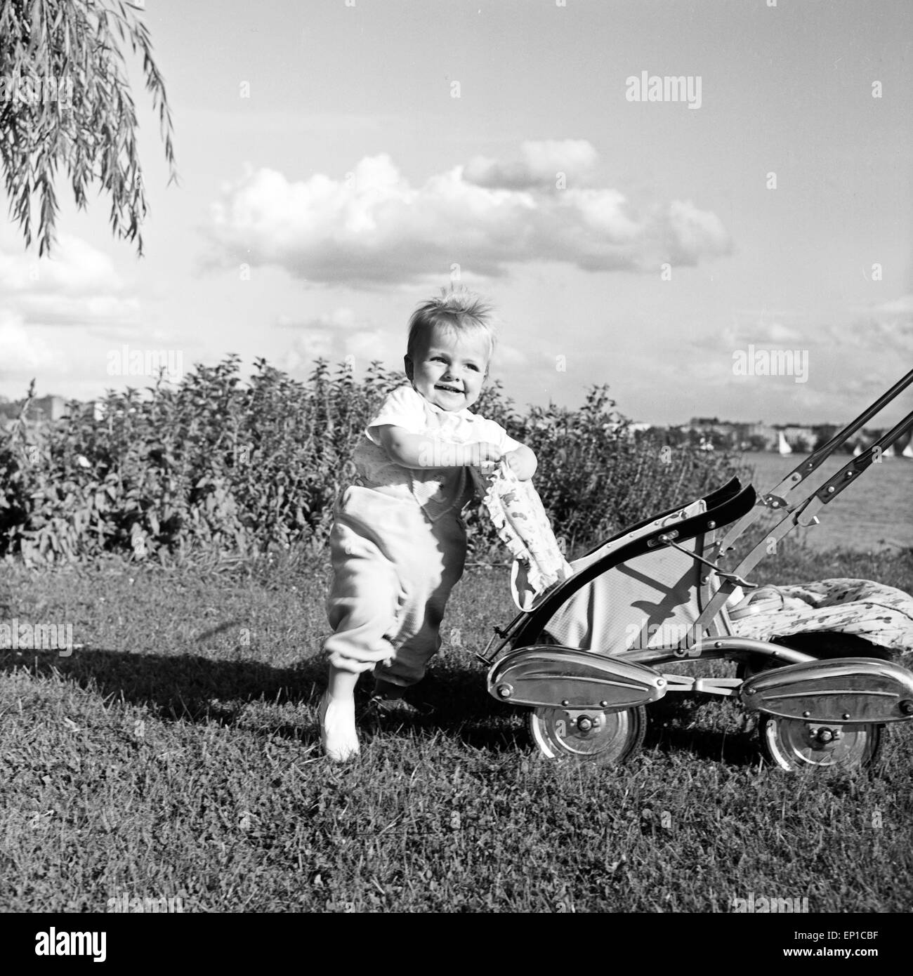 Ein Kleinkind mit seinem Sportwagen auf einer Wiese, Deutschland 1950er Jahre. A toddler with his pram on a lawn, Germany 1950s. Stock Photo