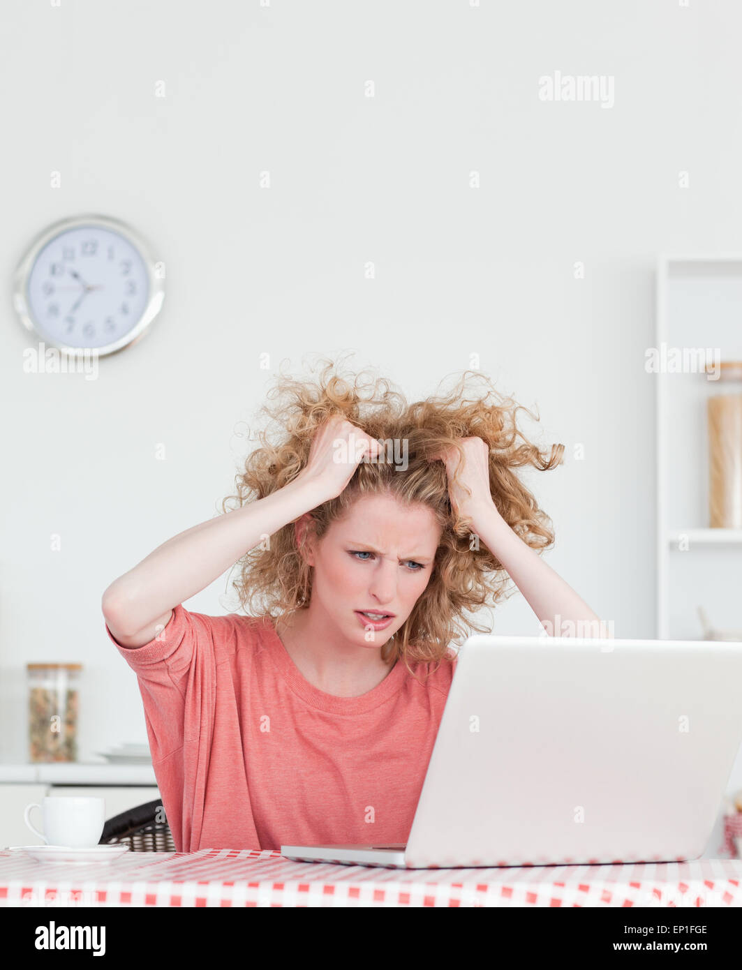 Attractive blonde female being angry while relaxing with her laptop in the kitchen Stock Photo