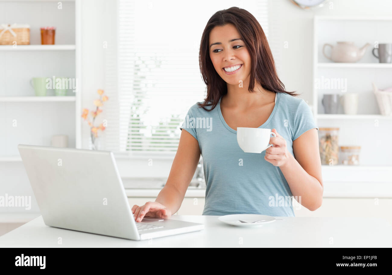 Beautiful woman enjoying a cup of coffee while relaxing with her laptop Stock Photo