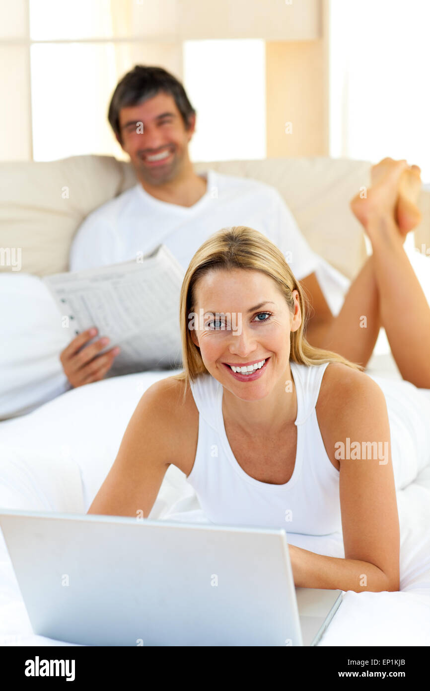 Smiling couple lying on bed using computer Stock Photo - Alamy