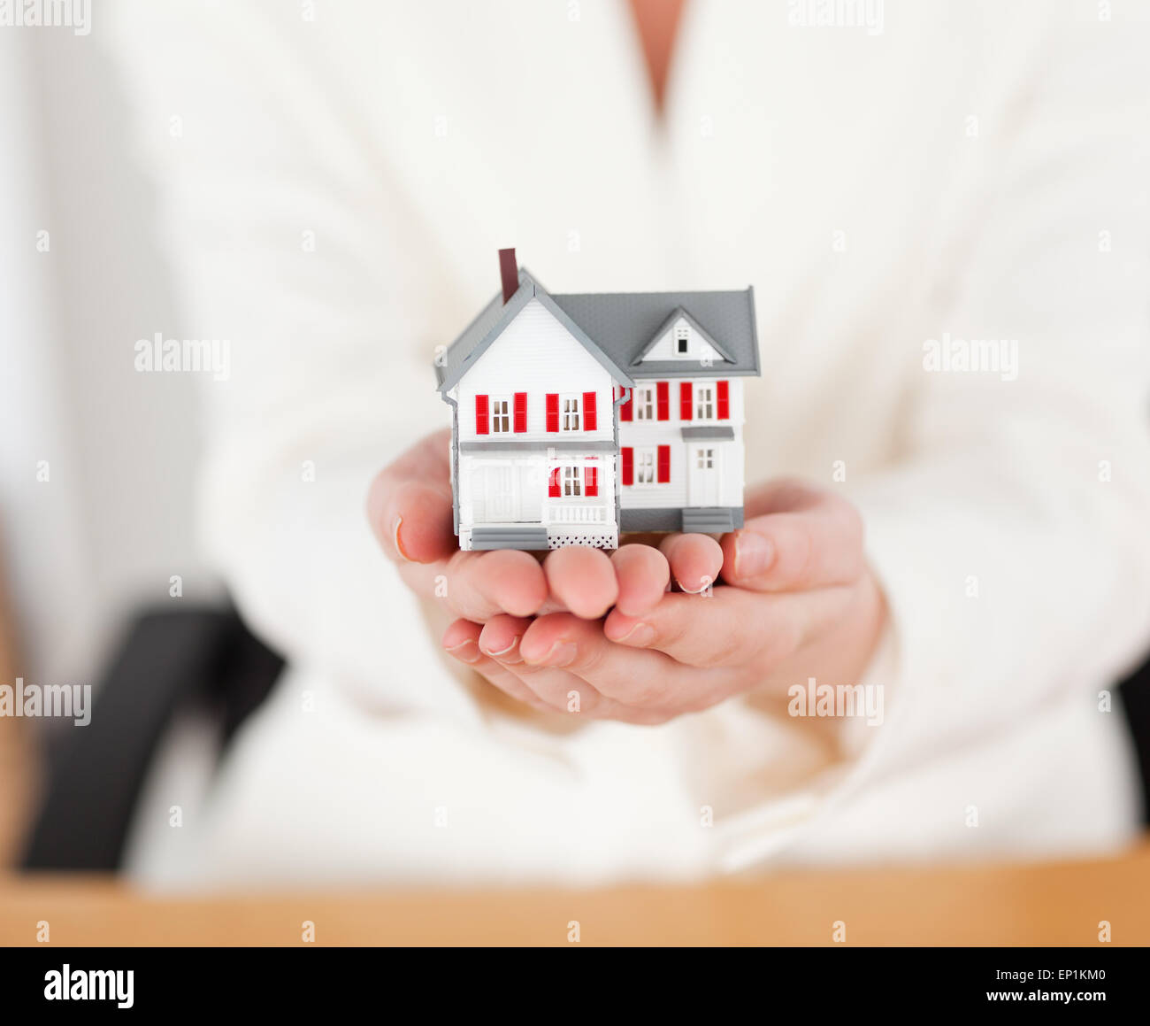 Young good looking red-haired female in suit holding a miniature house ...