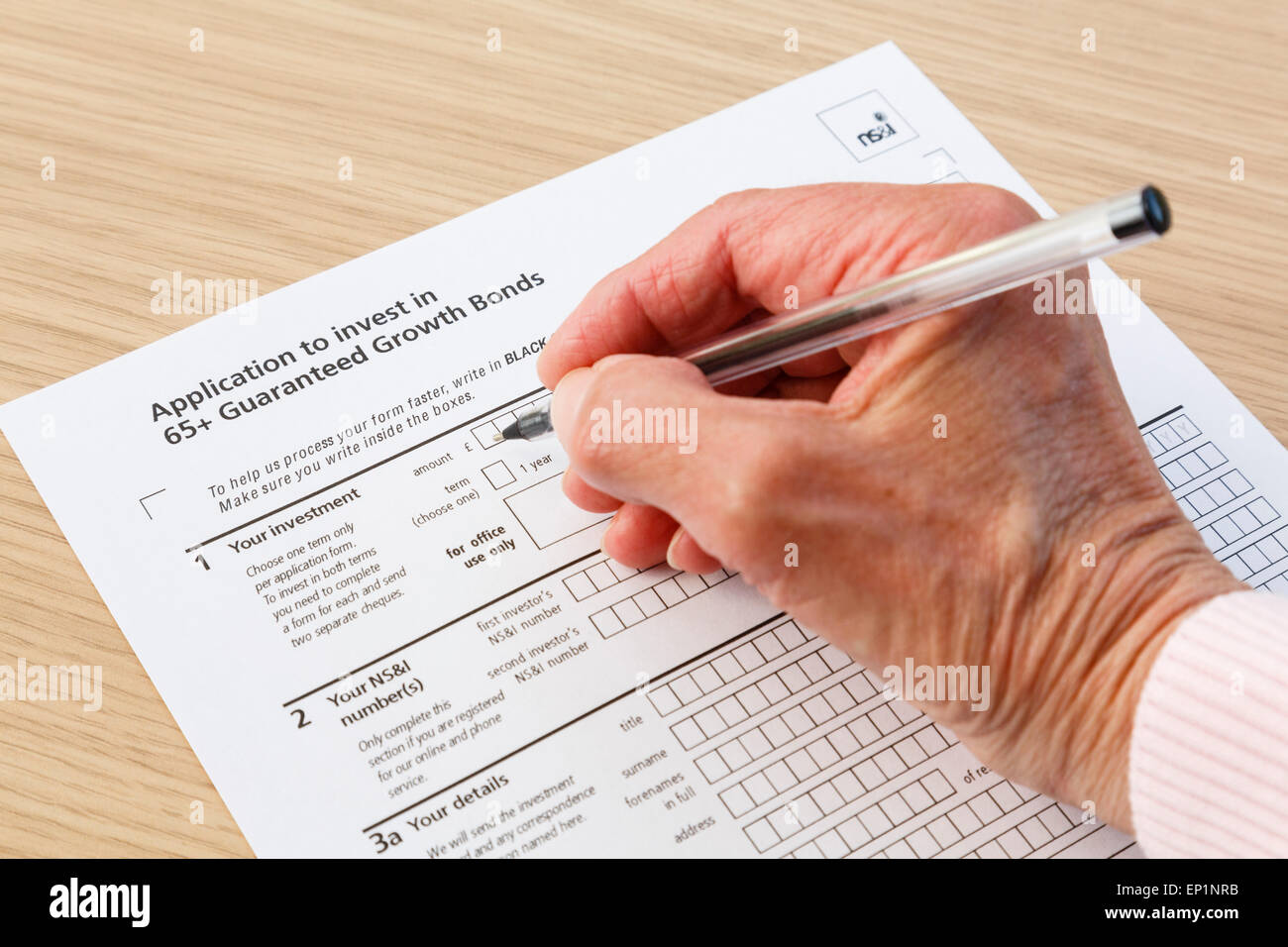 Elderly senior pensioner completing an application form to buy investments in 65+ Guaranteed Growth Bonds. England UK Britain Stock Photo