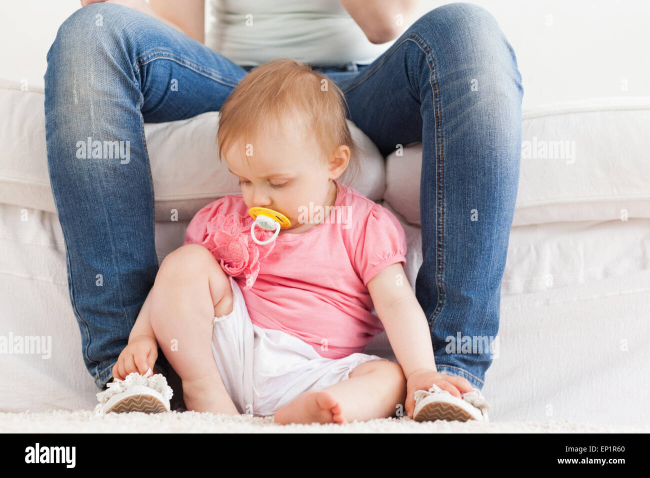 Baby playing with her mother's feet while sitting on a carpet Stock Photo