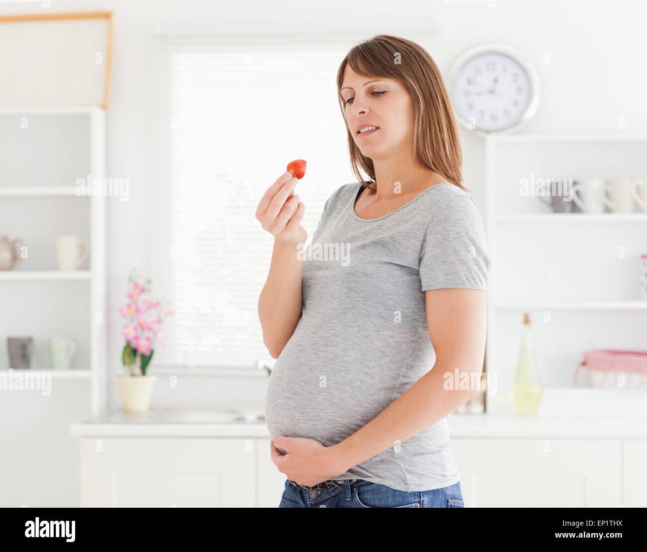 Good looking pregnant woman eating a strawberry while standing Stock