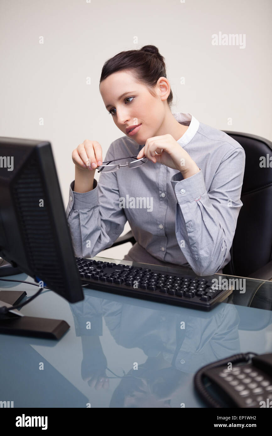 Businesswoman looking at screen holding her glasses Stock Photo