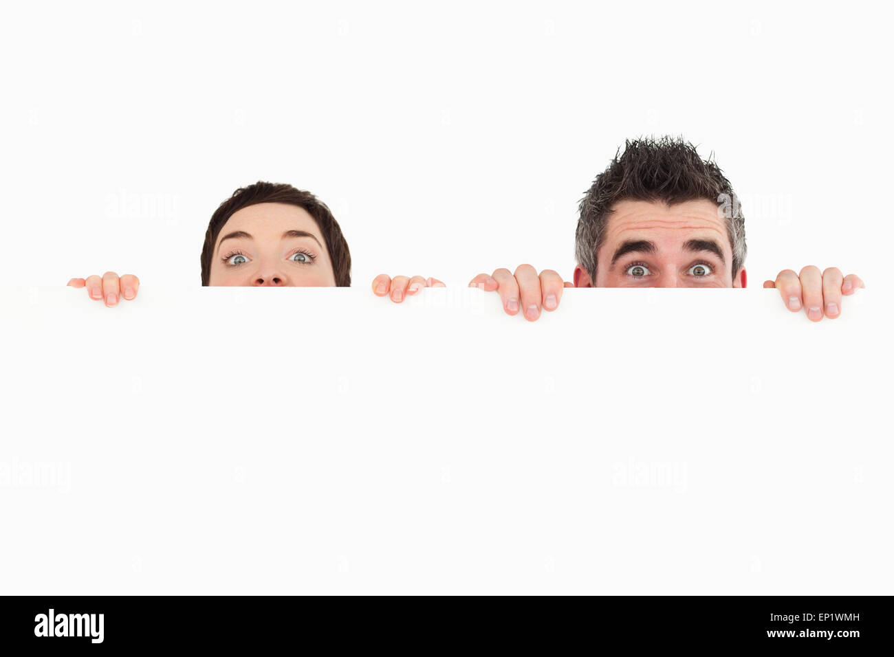 Man and woman hiding behind a white board with room for  copy sp Stock Photo