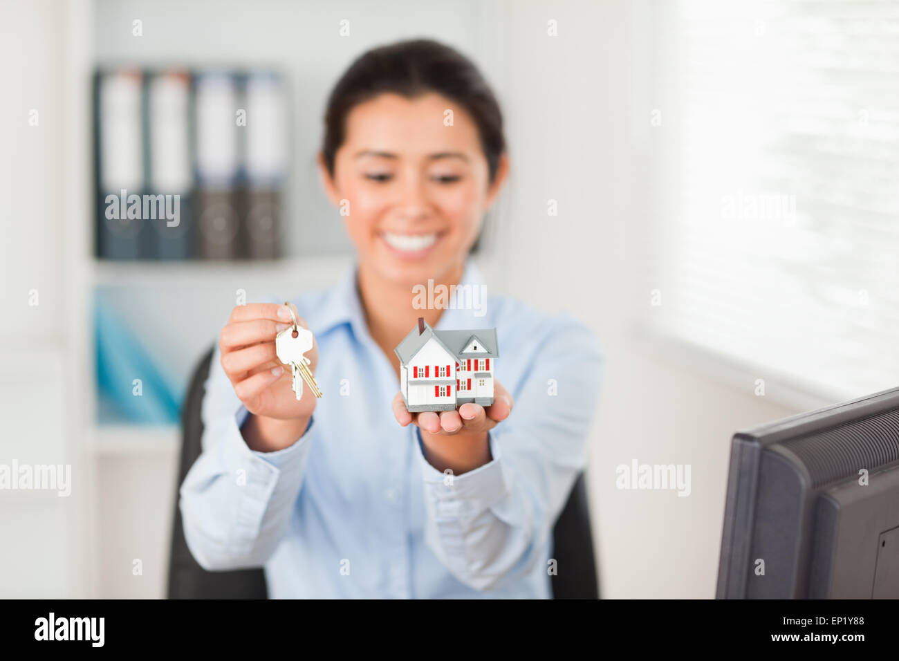Pretty woman holding keys and a miniature house while looking at the ...