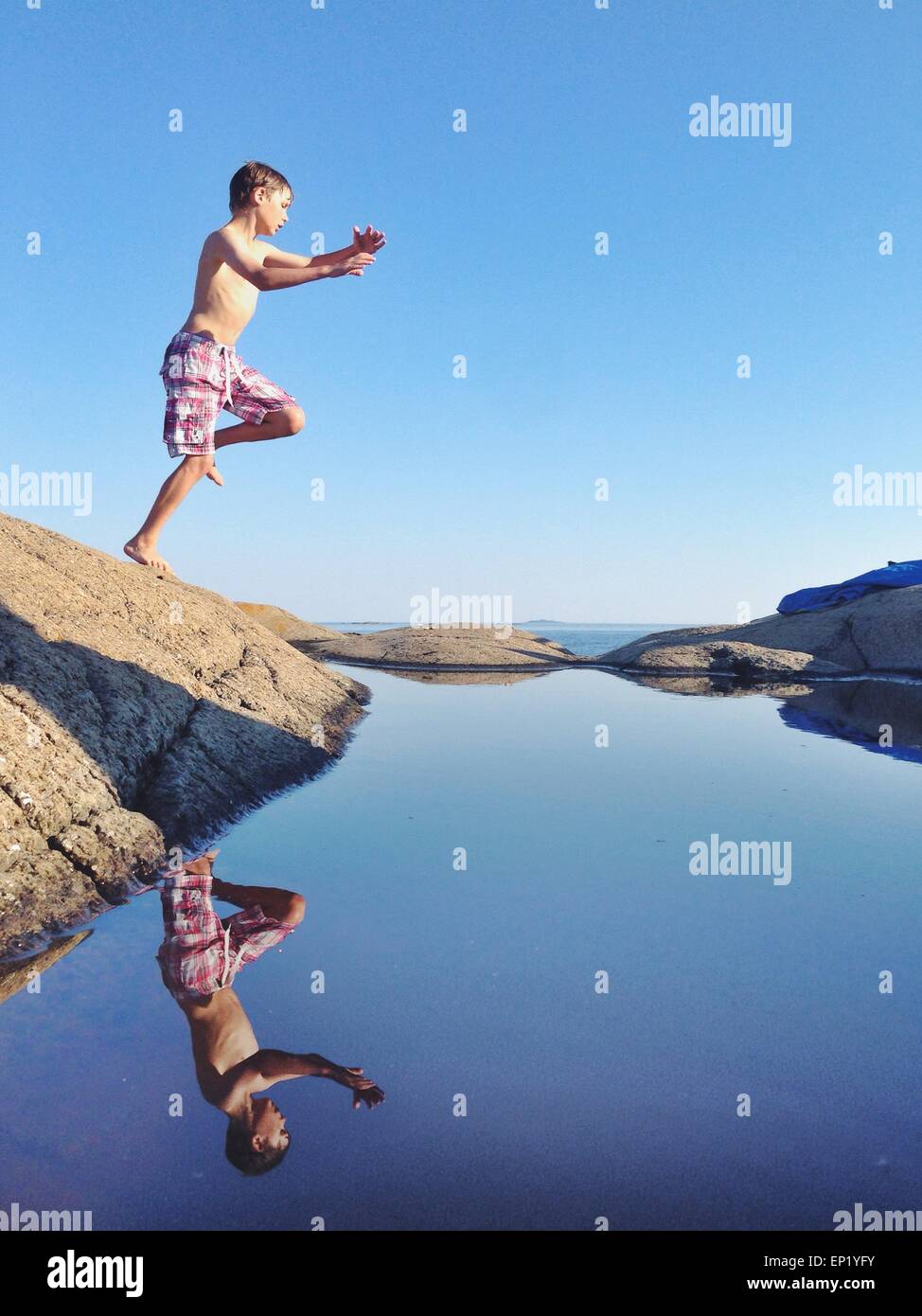 Boy jumping off a rock into the sea Stock Photo
