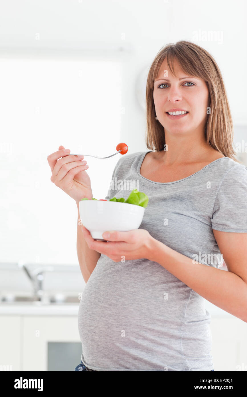 Pretty pregnant woman eating a cherry tomato while standing Stock Photo