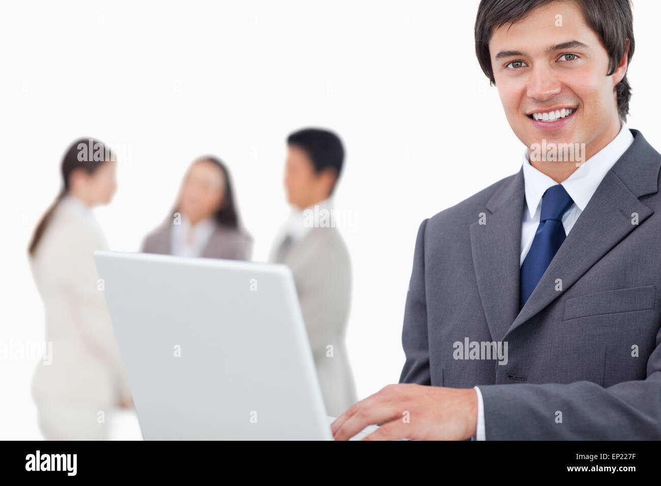 Smiling salesman with laptop and colleagues behind him Stock Photo - Alamy
