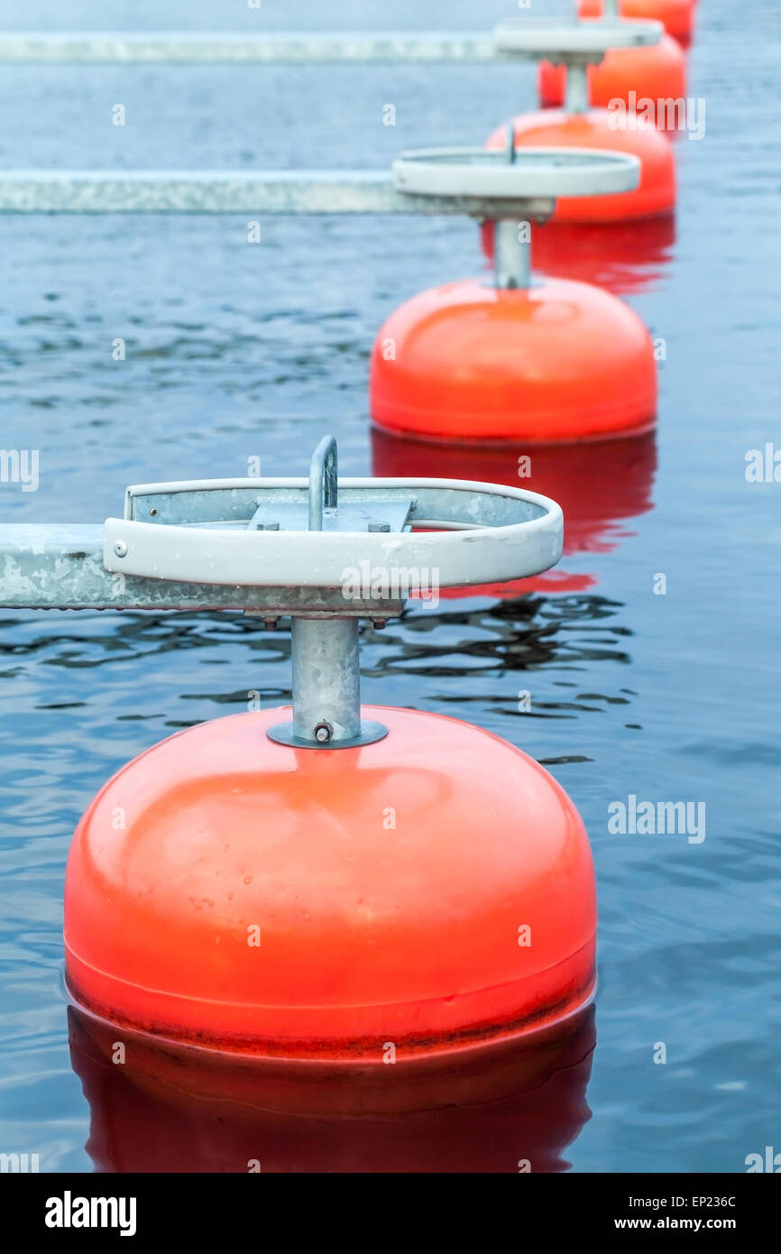 Red mooring buoys in a row floating on blue water, small European yacht