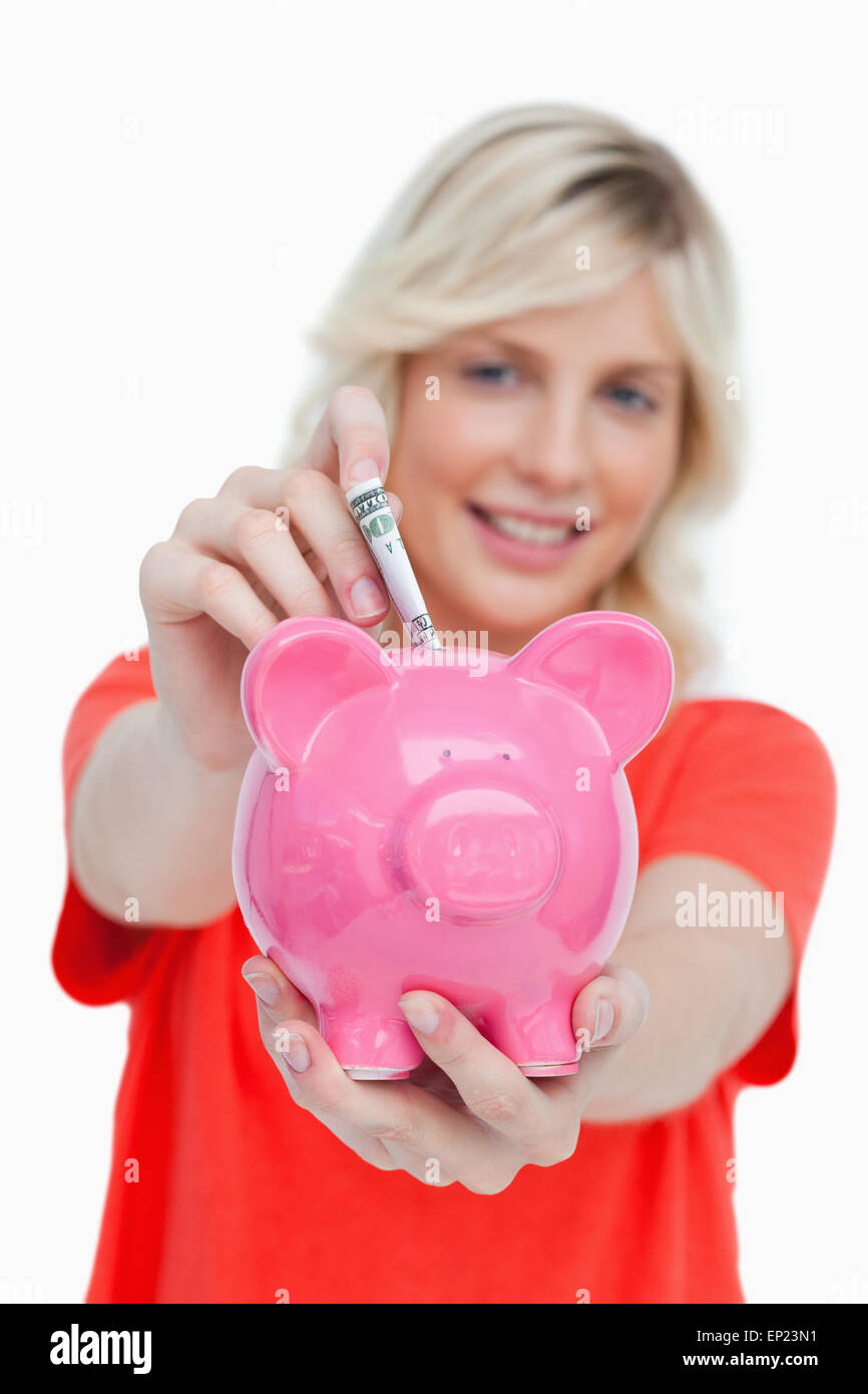 Young blonde woman putting notes into a pink piggy bank Stock Photo - Alamy