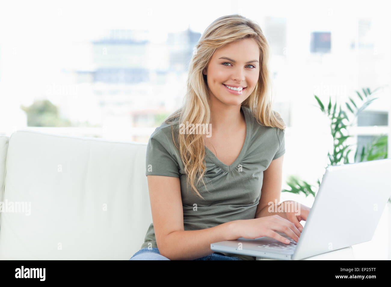 Woman smiling and looking forward as she uses a laptop on the couch ...