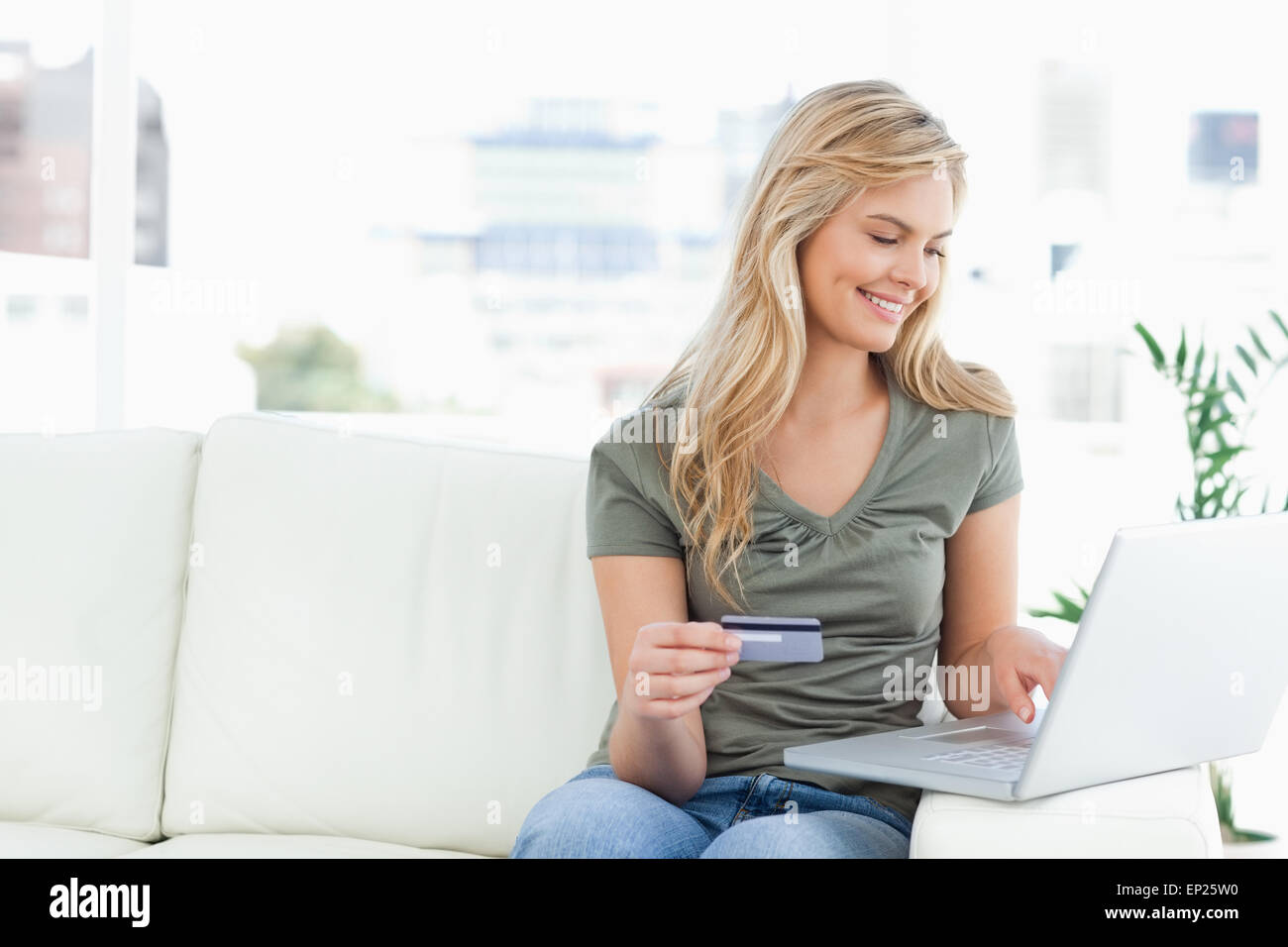 Woman smiles as she uses her laptop and credit card while sitting on ...