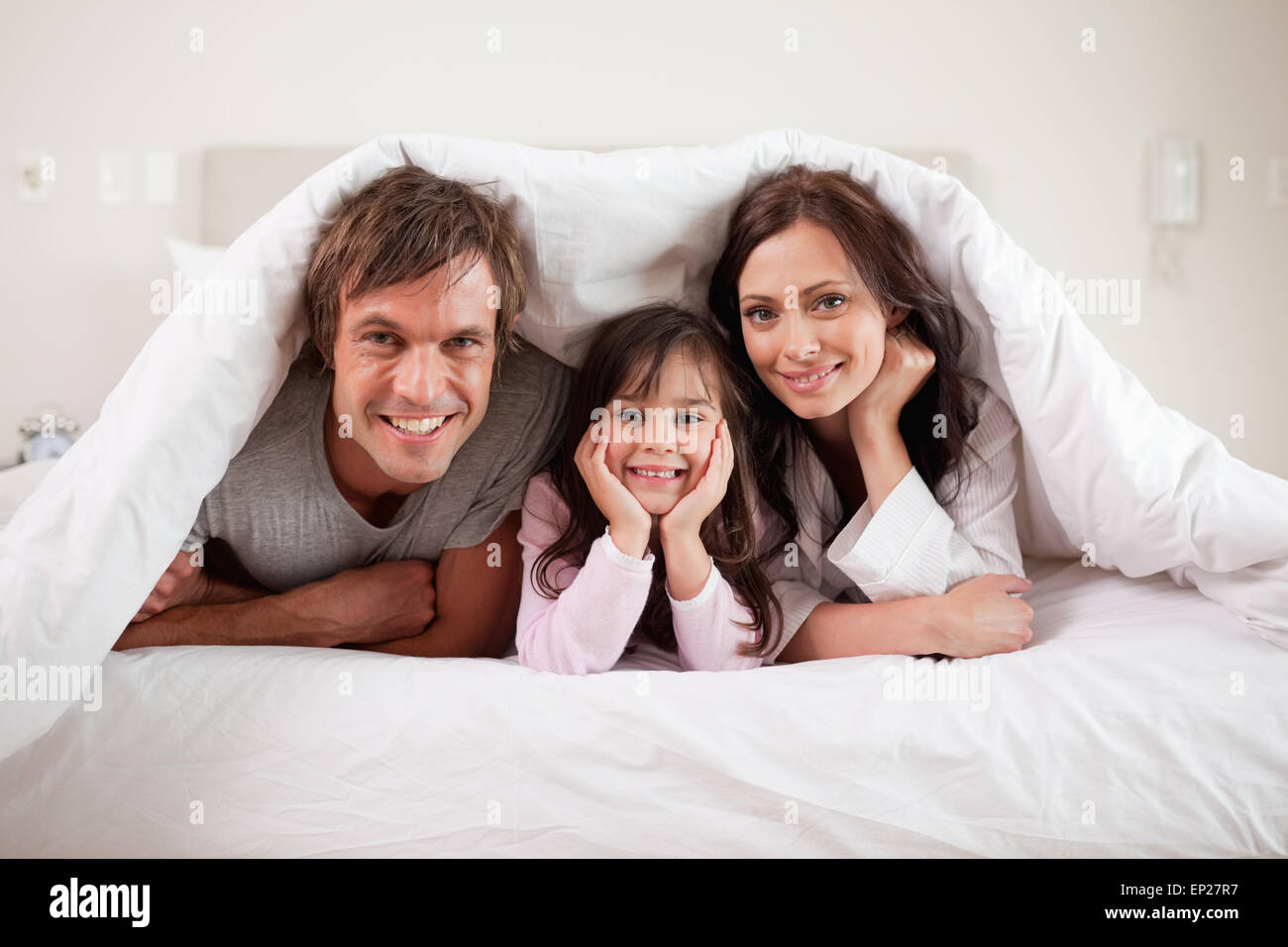 Smiling parents lying under a duvet with their daughter Stock Photo Alamy
