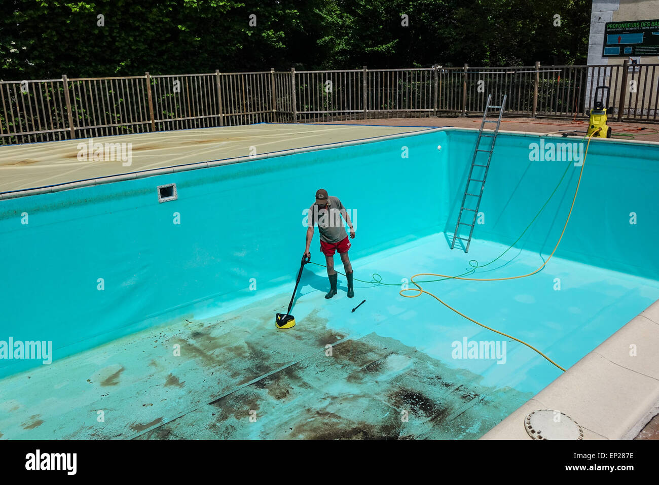 Karcher pressure washer power jet wash patio attachment being used by middle aged man wearing shorts to clean swimming pool walls and floor Stock Photo