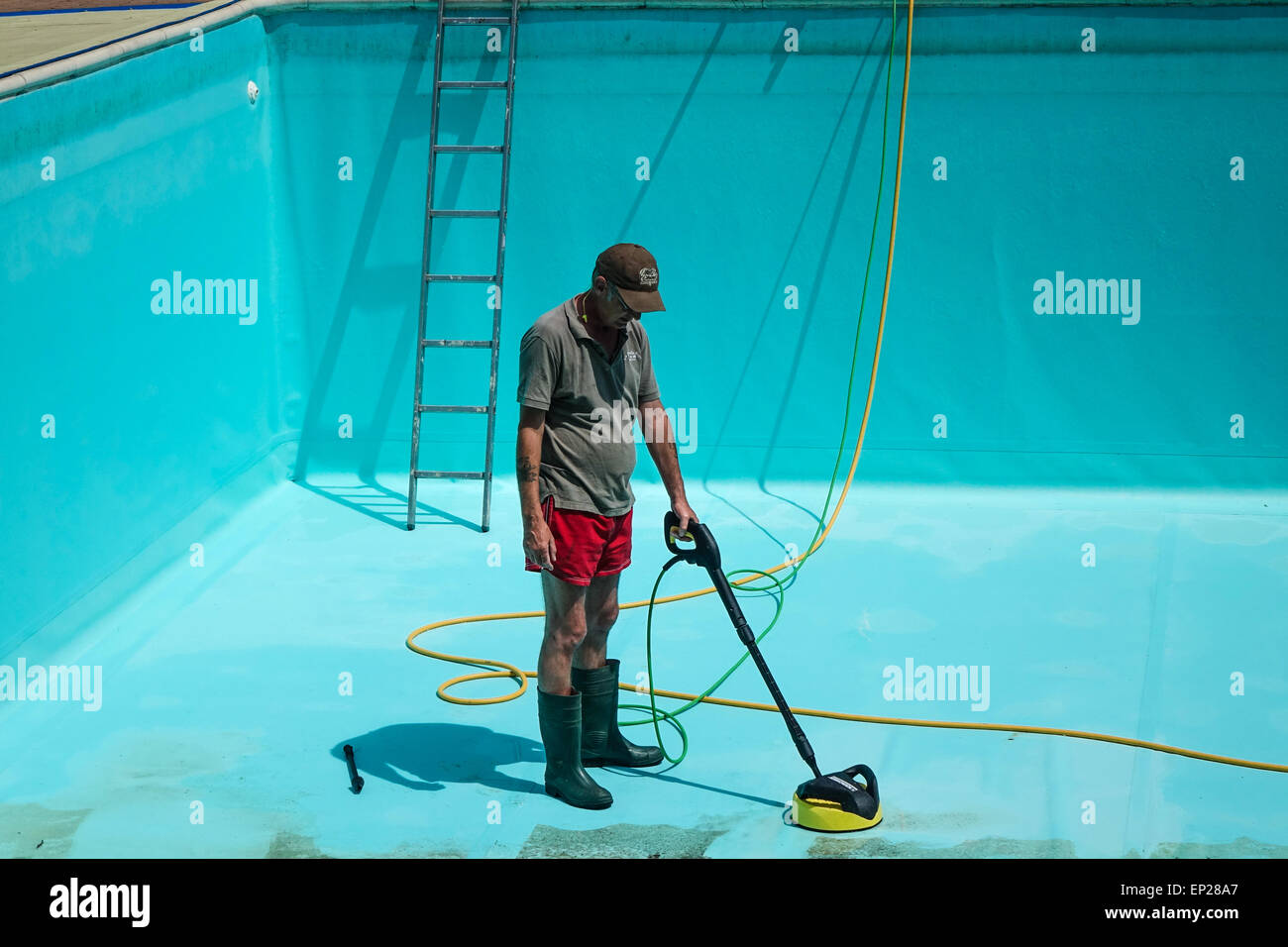 Karcher pressure washer power jet wash patio attachment being used by middle aged man wearing shorts to clean swimming pool walls and floor Stock Photo