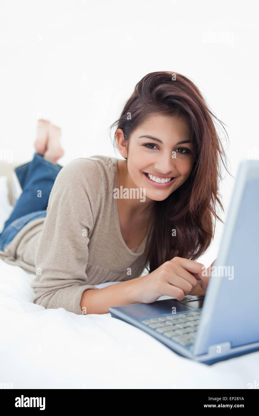 Woman smiling in front of her laptop, lying on the bed with her feet ...