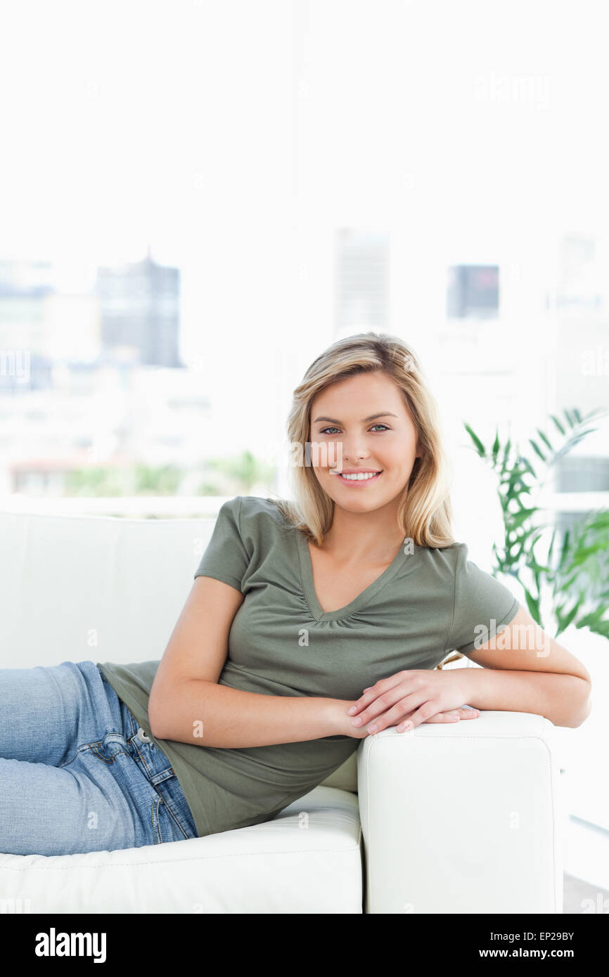 Woman lying across the couch, arms on the arm rest, smiling and looking
