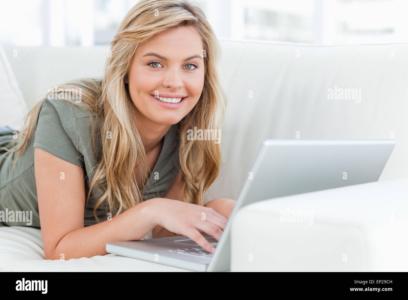 Woman lying across the couch, smiling as she looks forward, using her ...