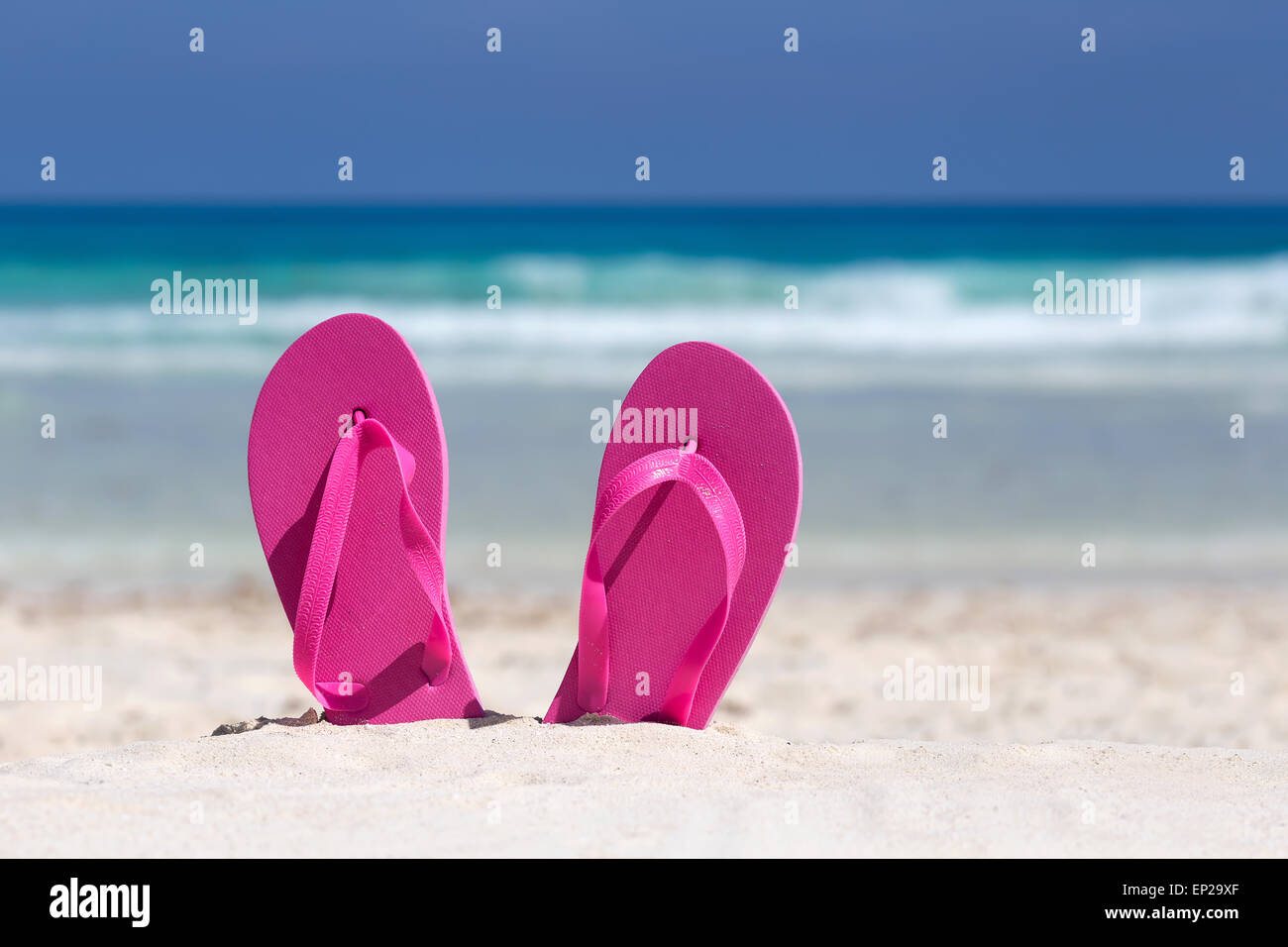 Pink flip flops on white sandy beach near sea waves, nobody. Summer vacation concept Stock Photo