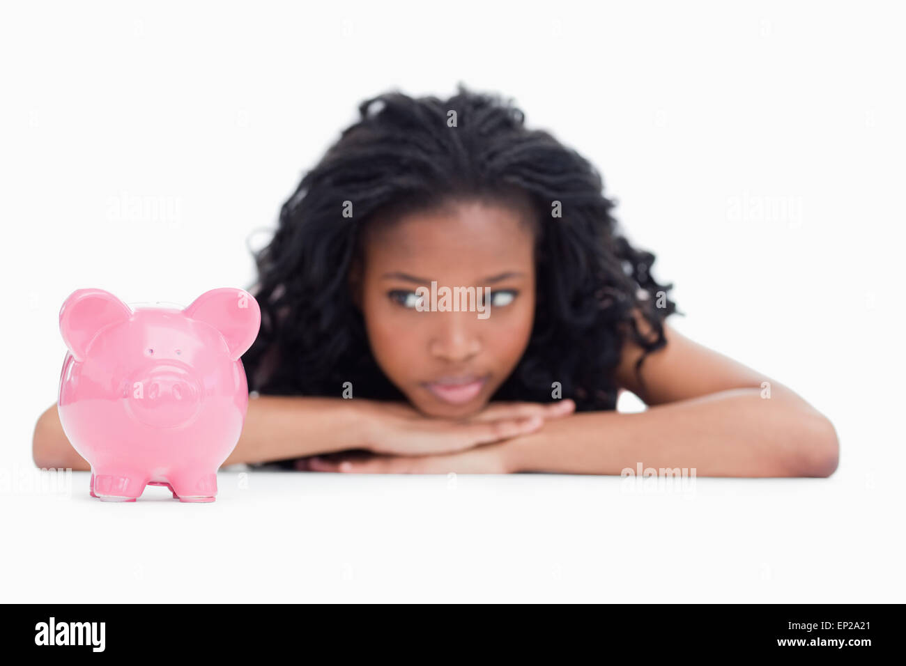 Young woman lying down resting her head on her hands is looking at a piggy bank Stock Photo