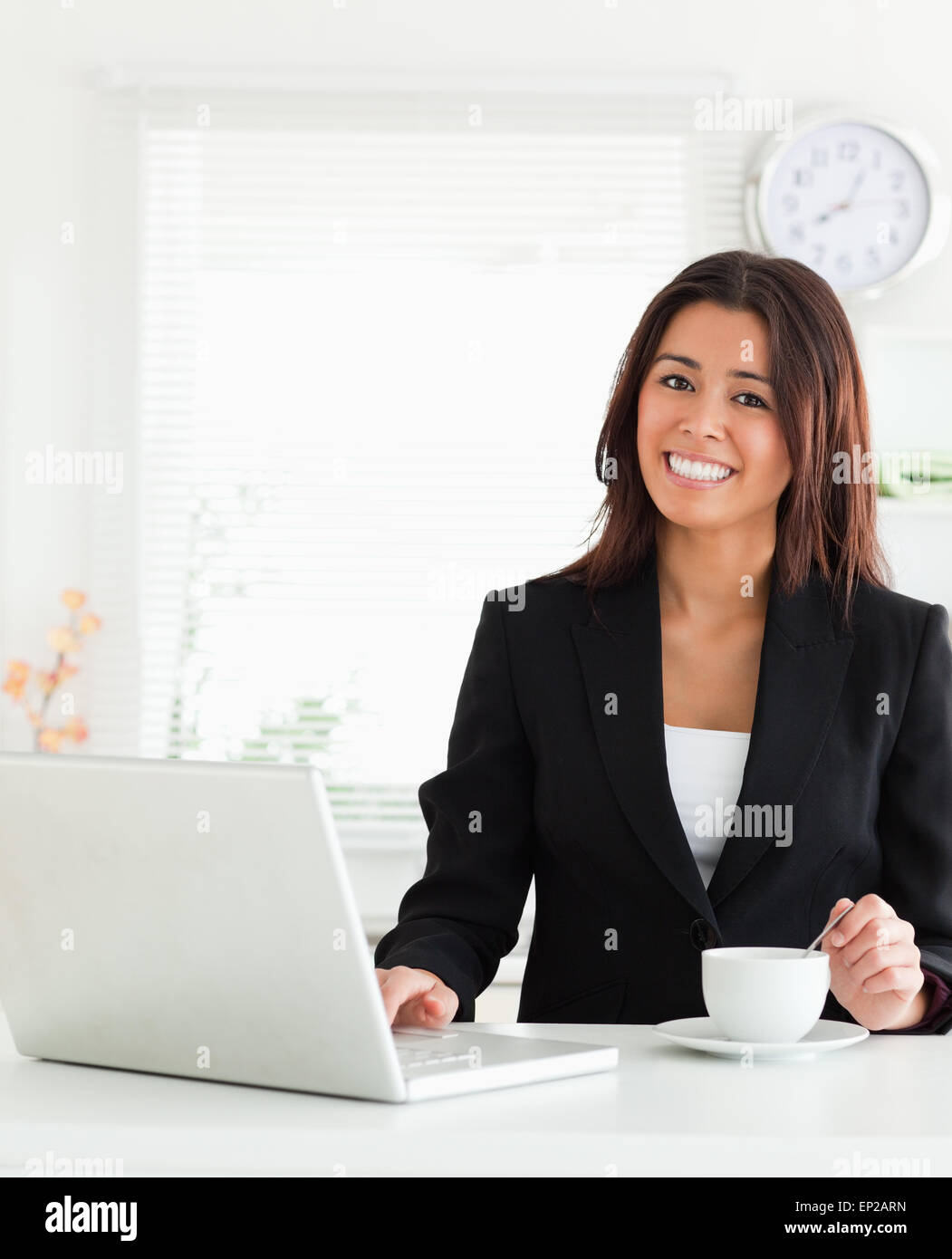 Good looking woman in suit enjoying a cup of coffee while relaxing with her laptop Stock Photo