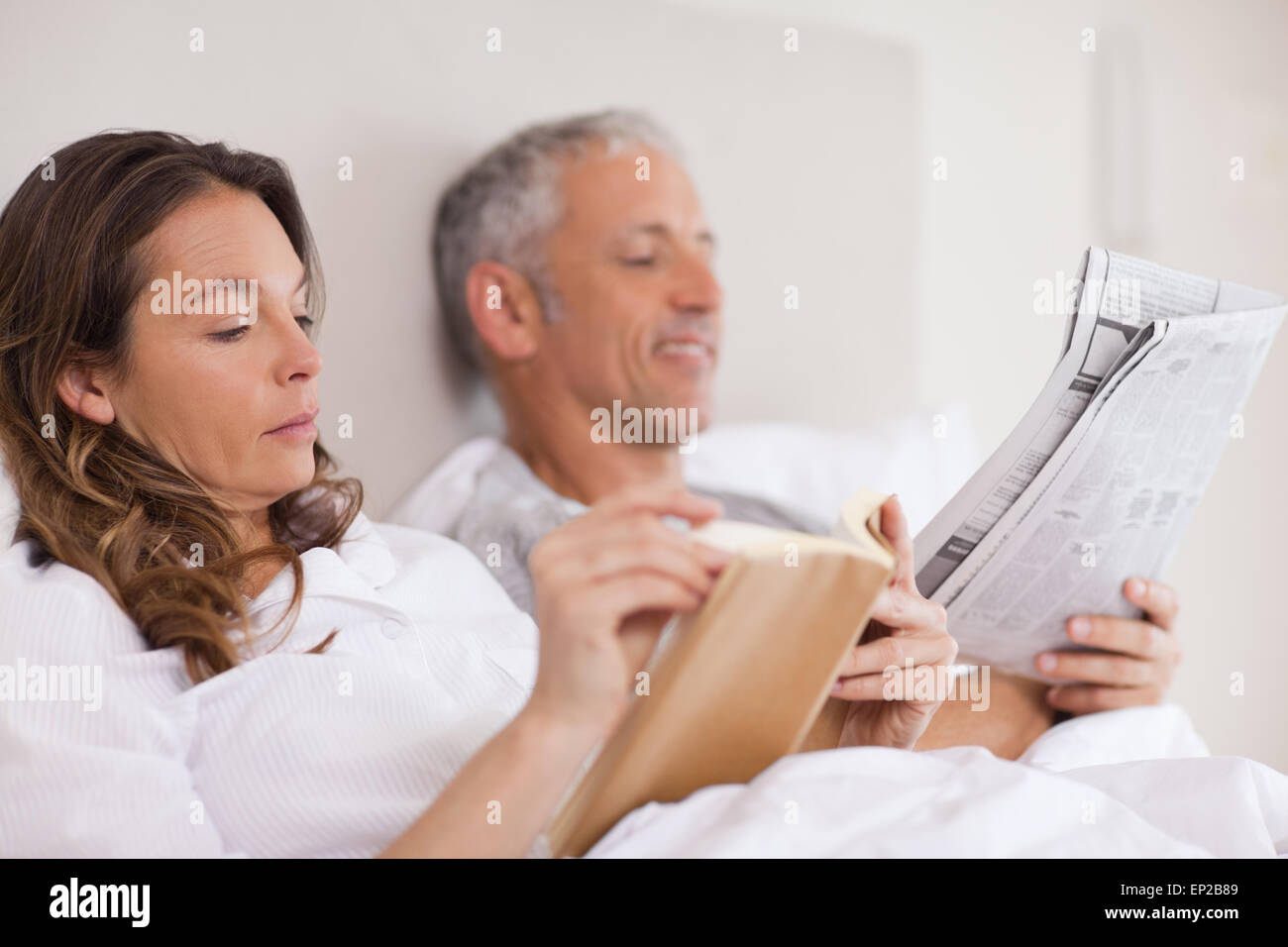 Woman reading a book while her husband is reading a newspaper Stock Photo