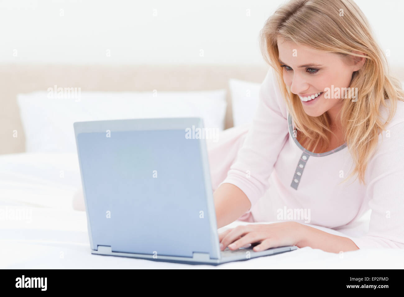 Woman lying on the bed, using a laptop and smiling Stock Photo - Alamy