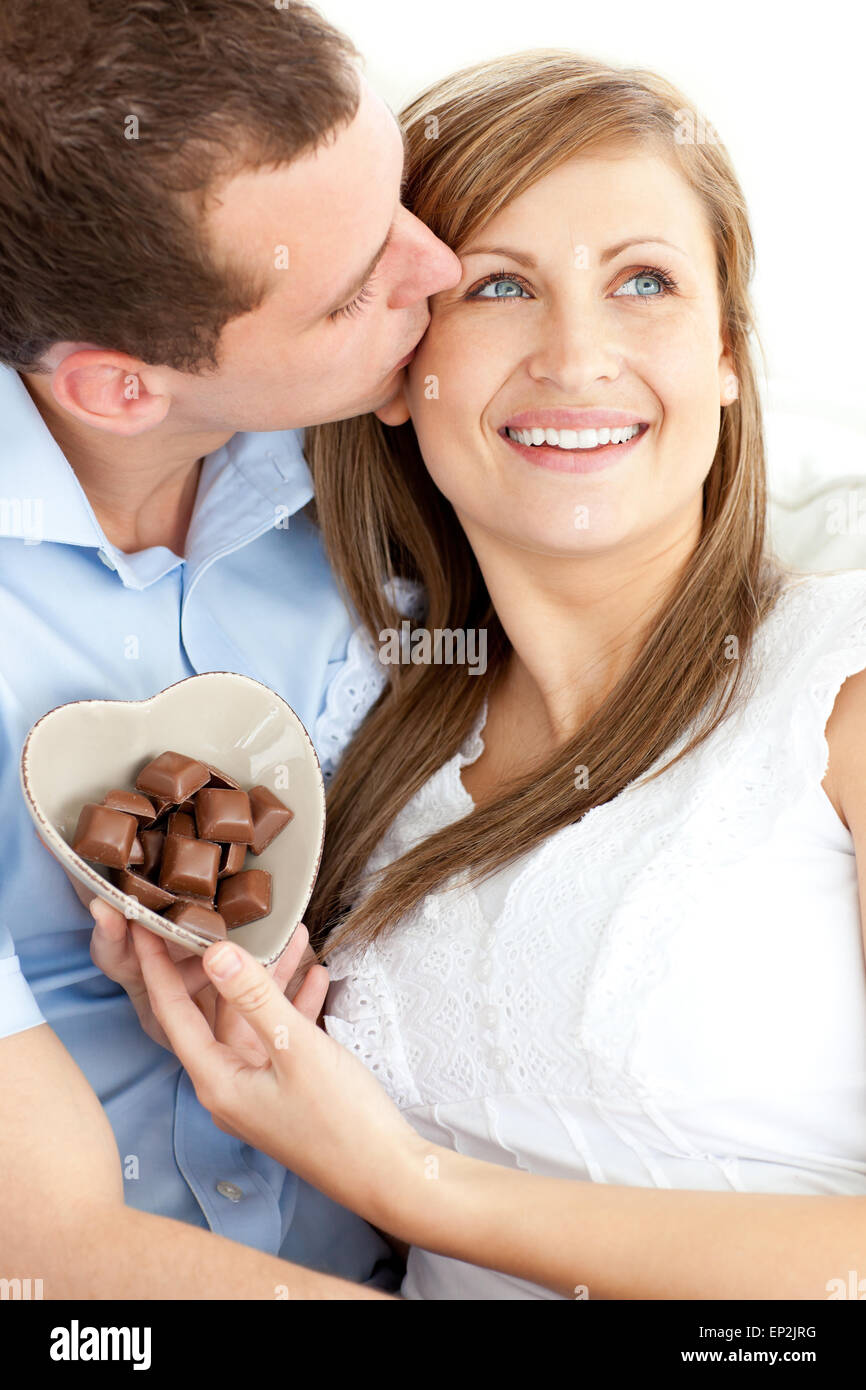Handsome man kissing his girlfriend holding chocolote sitting against
