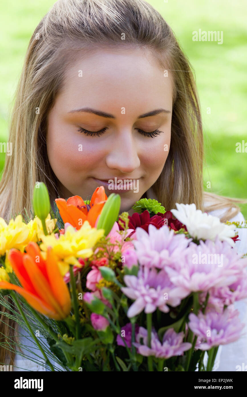 Young blonde girl closing her eyes while smelling a bunch of flowers ...